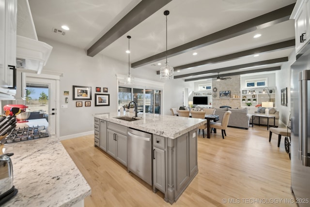 kitchen featuring light stone countertops, stainless steel appliances, ceiling fan, sink, and a center island with sink