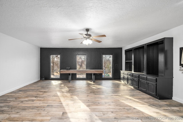 unfurnished living room with light wood-style floors, a textured ceiling, baseboards, and a ceiling fan