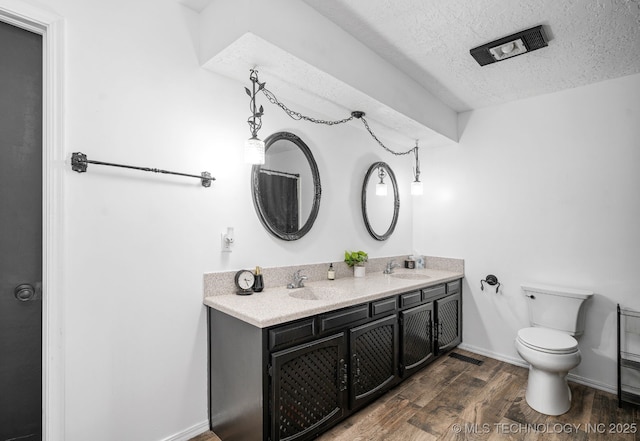 bathroom with a textured ceiling, toilet, wood finished floors, a sink, and double vanity