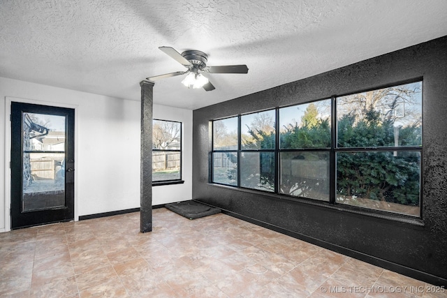 empty room with ceiling fan, baseboards, a textured ceiling, and a textured wall