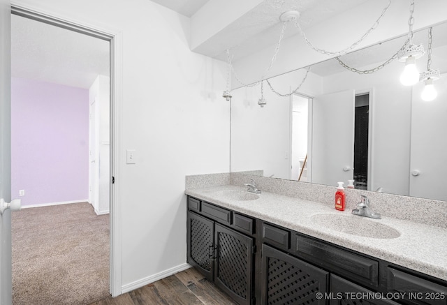 bathroom with wood finished floors, a sink, baseboards, and double vanity