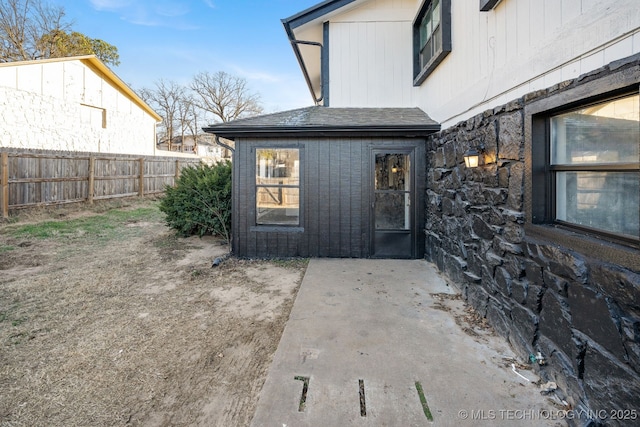 doorway to property with a patio area, fence, and roof with shingles