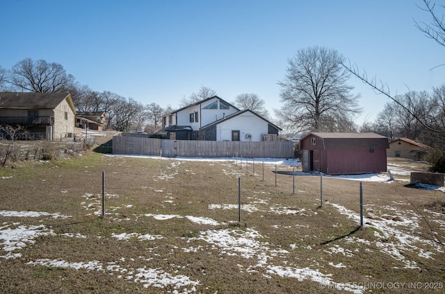 yard layered in snow featuring an outbuilding, a storage unit, and fence