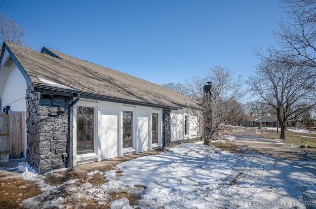 snow covered property featuring stone siding and a chimney