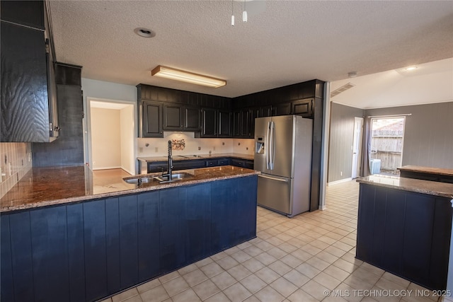 kitchen with sink, stainless steel fridge with ice dispenser, kitchen peninsula, dark stone countertops, and a textured ceiling