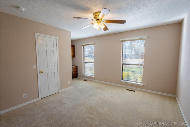 unfurnished room with a textured ceiling, light colored carpet, plenty of natural light, and ceiling fan