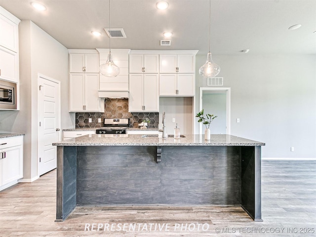 kitchen featuring hanging light fixtures, appliances with stainless steel finishes, light stone counters, and a kitchen island with sink