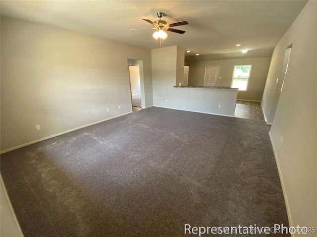 unfurnished living room with ceiling fan and dark carpet