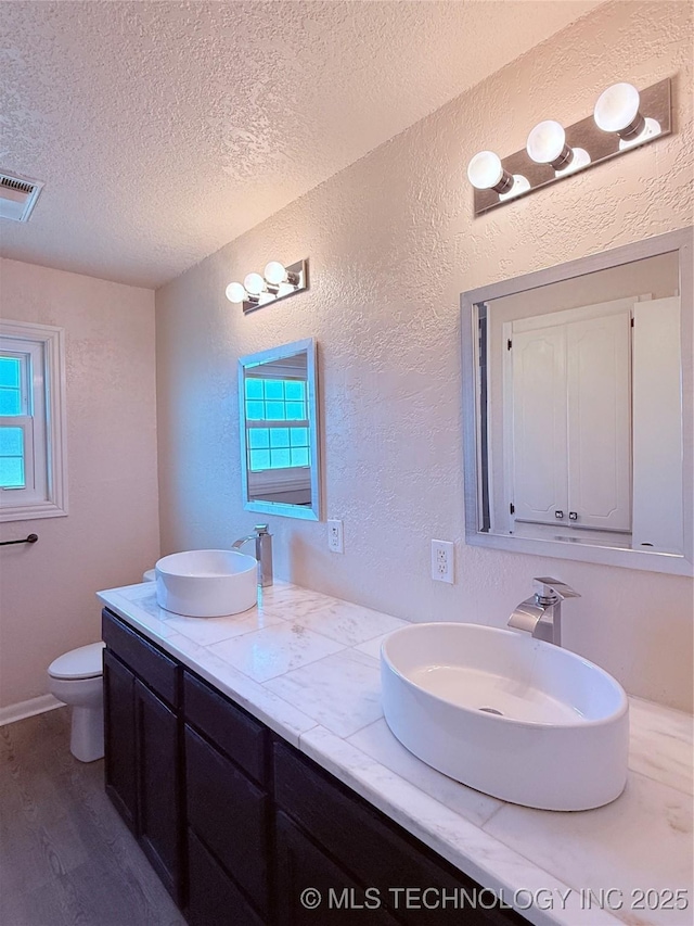 bathroom with vanity, toilet, a textured ceiling, and a wealth of natural light