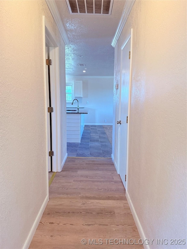 corridor with crown molding, light hardwood / wood-style floors, and a textured ceiling