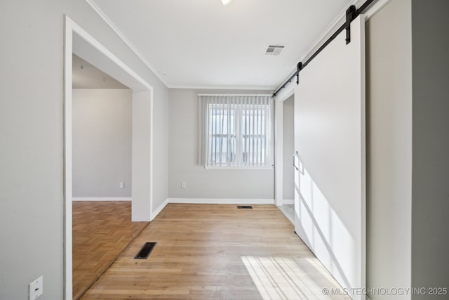 unfurnished room with a barn door, crown molding, and light hardwood / wood-style floors