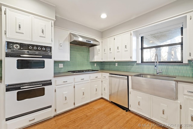 kitchen featuring sink, range hood, appliances with stainless steel finishes, white cabinets, and light wood-type flooring