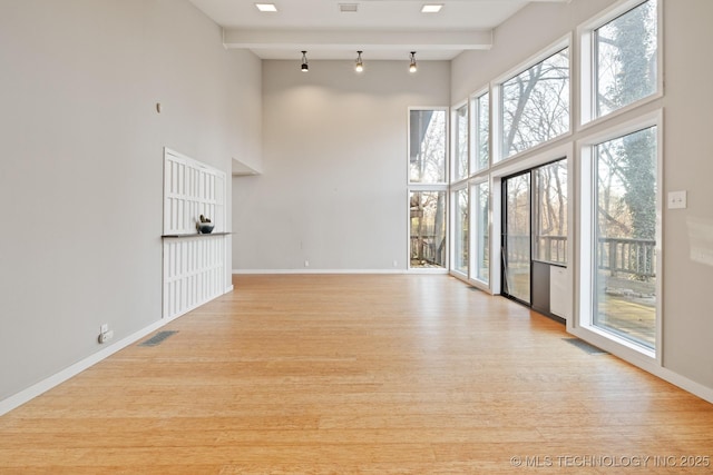 unfurnished living room featuring beam ceiling, a towering ceiling, and light hardwood / wood-style floors