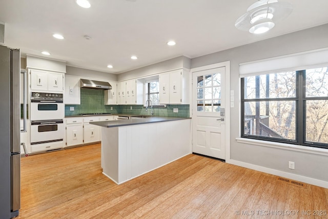 kitchen featuring stainless steel fridge, white cabinetry, kitchen peninsula, and extractor fan