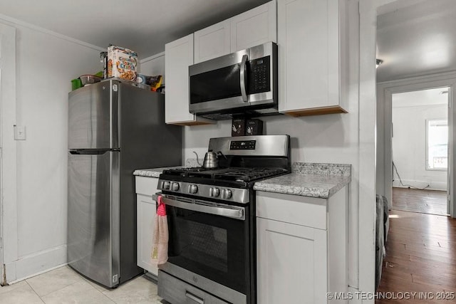 kitchen featuring crown molding, white cabinetry, stainless steel appliances, and light tile patterned floors