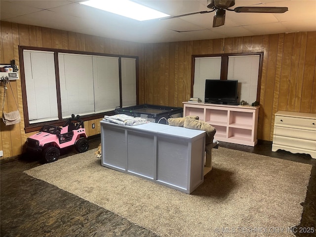 living room with ceiling fan, wood walls, and dark carpet