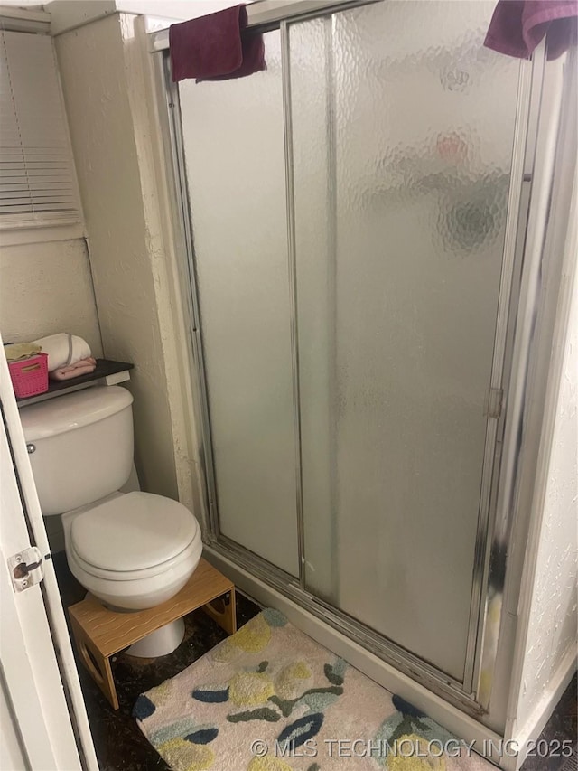 bathroom with a shower with shower door and toilet