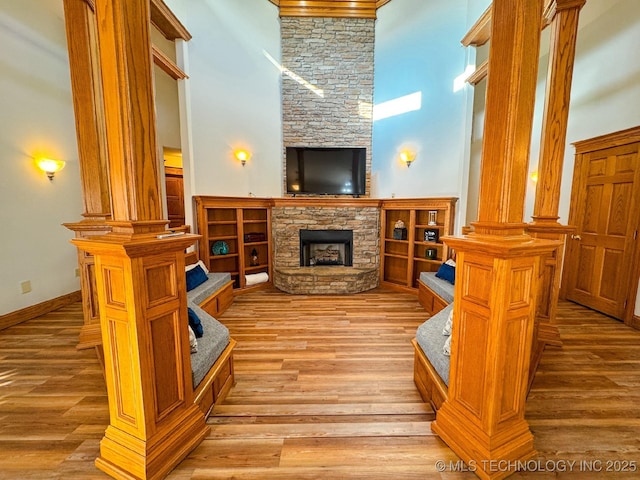 living room with ornate columns, a high ceiling, a fireplace, and light hardwood / wood-style floors