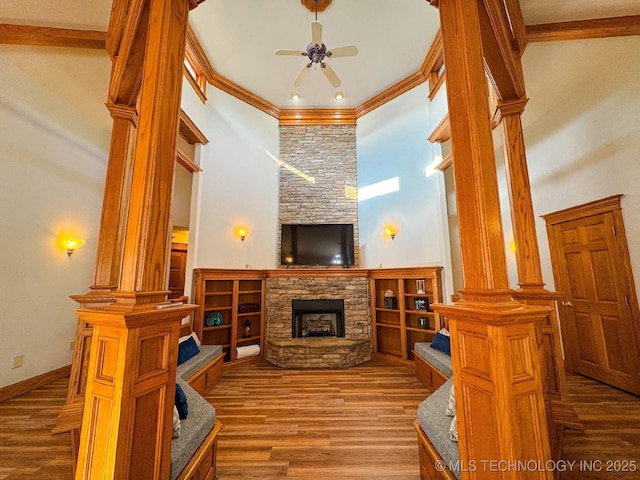 living room featuring a stone fireplace, crown molding, a towering ceiling, hardwood / wood-style flooring, and ceiling fan