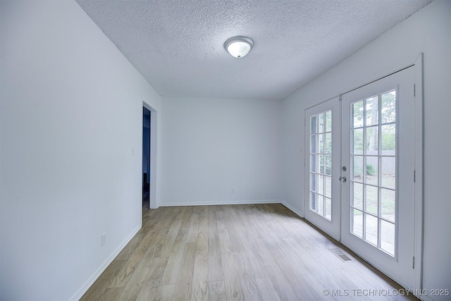 spare room with french doors, a textured ceiling, and light hardwood / wood-style flooring