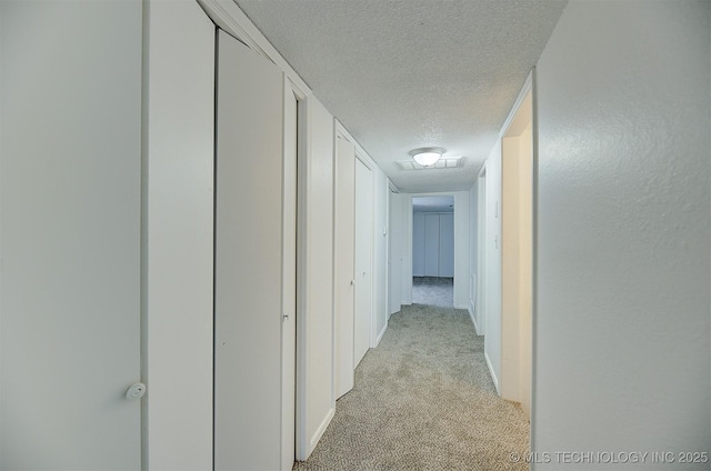 hallway with a textured ceiling and light carpet