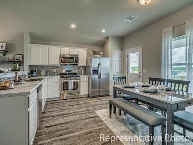 kitchen with appliances with stainless steel finishes, backsplash, light wood-type flooring, sink, and white cabinets