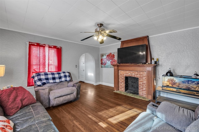 living room featuring a fireplace, ceiling fan, crown molding, and dark wood-type flooring