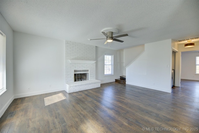 unfurnished living room featuring ceiling fan, a healthy amount of sunlight, dark wood-type flooring, and a brick fireplace