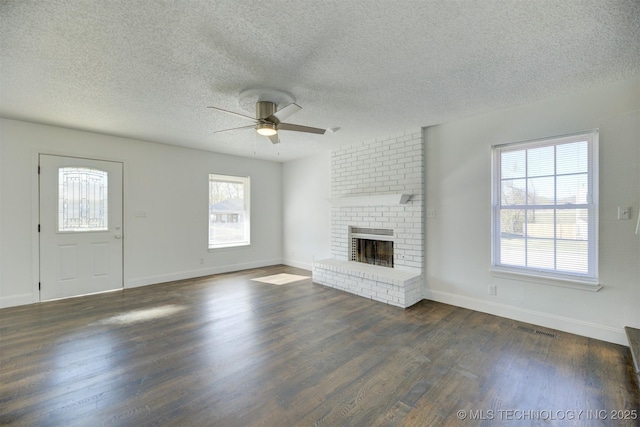 unfurnished living room featuring ceiling fan, a textured ceiling, a wealth of natural light, and a brick fireplace