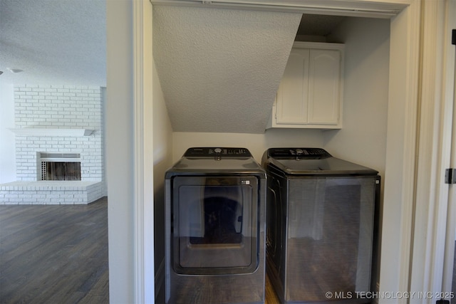 laundry area with cabinets, wood-type flooring, washing machine and dryer, and a brick fireplace