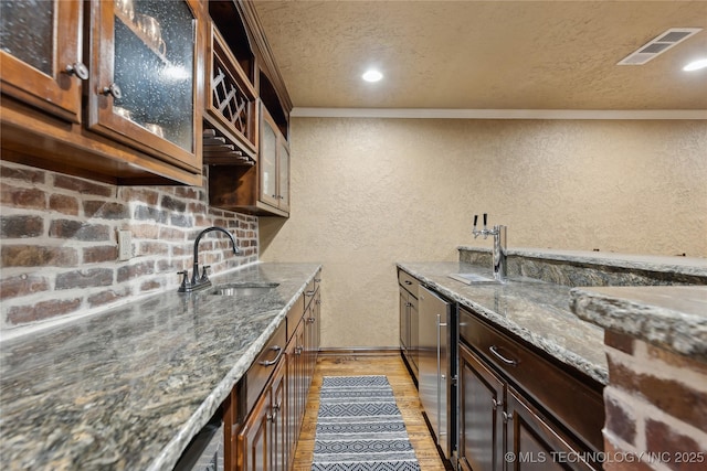 kitchen featuring dark brown cabinets, crown molding, sink, dark stone countertops, and light hardwood / wood-style floors