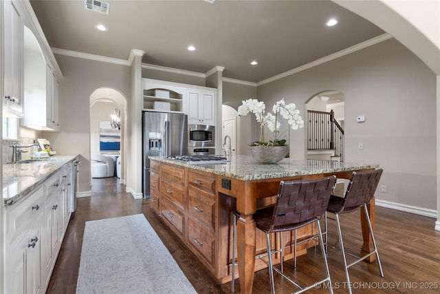 kitchen with white cabinets, sink, light stone counters, and an island with sink