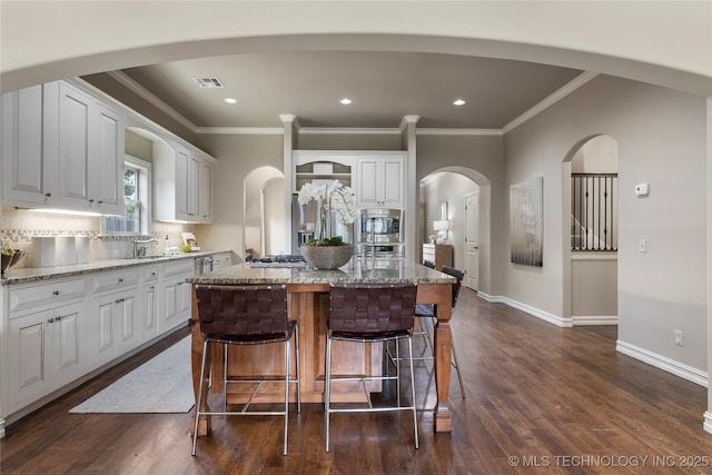 kitchen with light stone countertops, tasteful backsplash, dark wood-type flooring, a center island, and white cabinetry