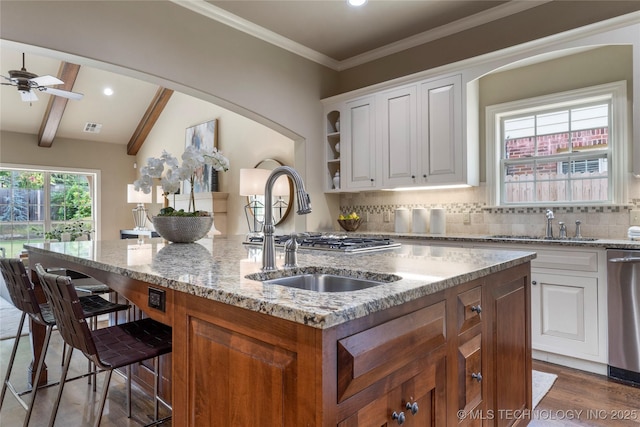 kitchen featuring stainless steel dishwasher, sink, lofted ceiling with beams, white cabinetry, and an island with sink