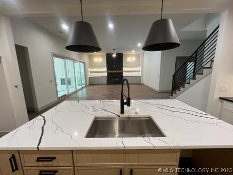 kitchen with light stone counters, sink, hanging light fixtures, and a center island with sink