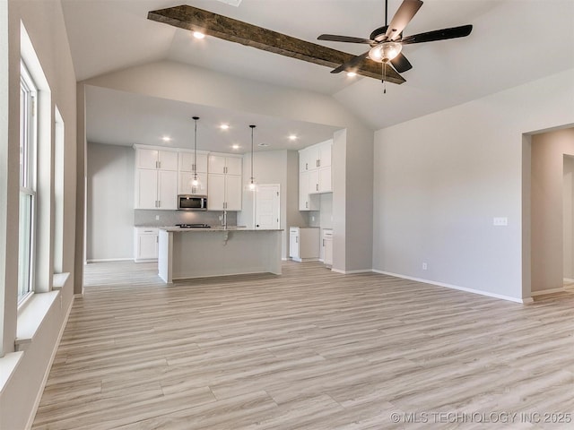 kitchen with ceiling fan, light stone counters, an island with sink, decorative light fixtures, and white cabinets