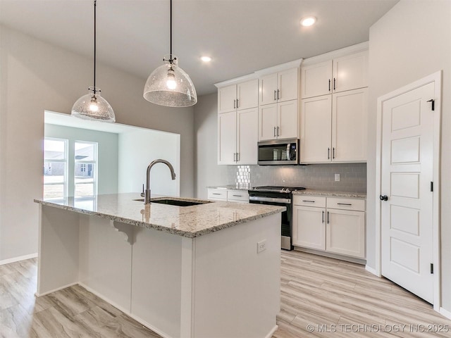 kitchen featuring sink, stainless steel appliances, decorative light fixtures, a kitchen island with sink, and white cabinets