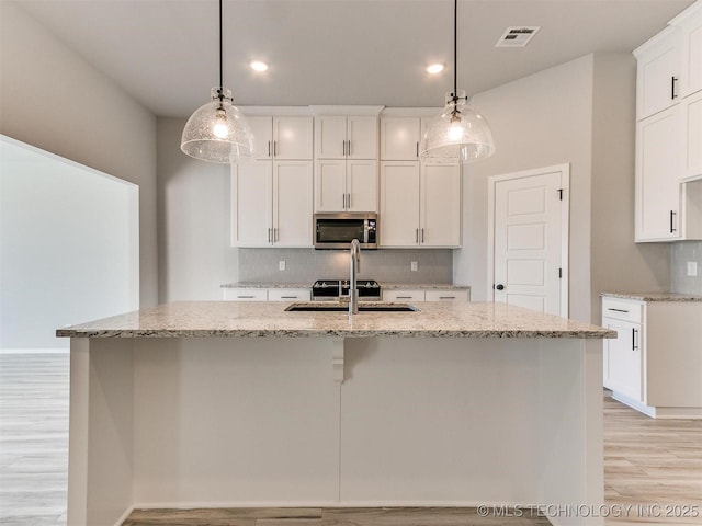 kitchen with a center island with sink, pendant lighting, white cabinetry, and sink