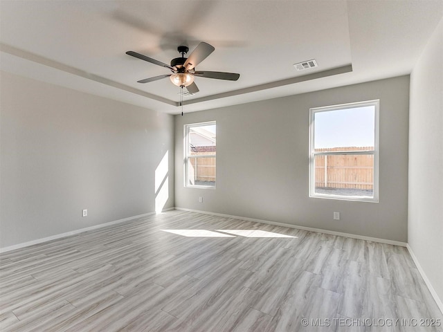 empty room with ceiling fan, light hardwood / wood-style floors, and a tray ceiling