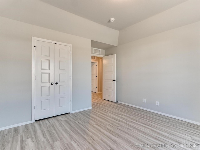 unfurnished bedroom with a closet, light hardwood / wood-style floors, and lofted ceiling