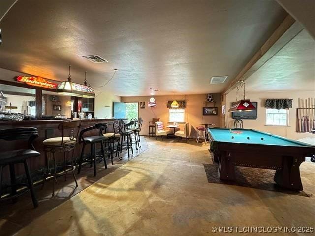 playroom with bar, a healthy amount of sunlight, concrete floors, and billiards