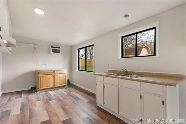 kitchen with white cabinets, light hardwood / wood-style floors, sink, and a wall unit AC