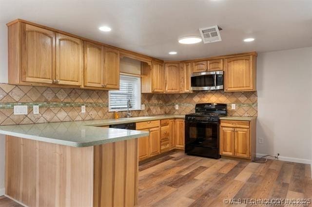 kitchen featuring kitchen peninsula, light hardwood / wood-style flooring, black gas range oven, and sink