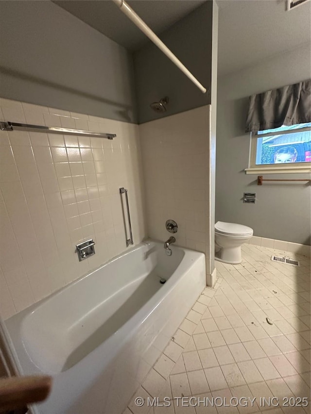 bathroom with tiled shower / bath combo, tile patterned floors, and toilet