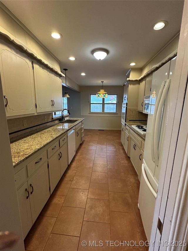 kitchen featuring sink, white appliances, white cabinetry, hanging light fixtures, and light stone countertops