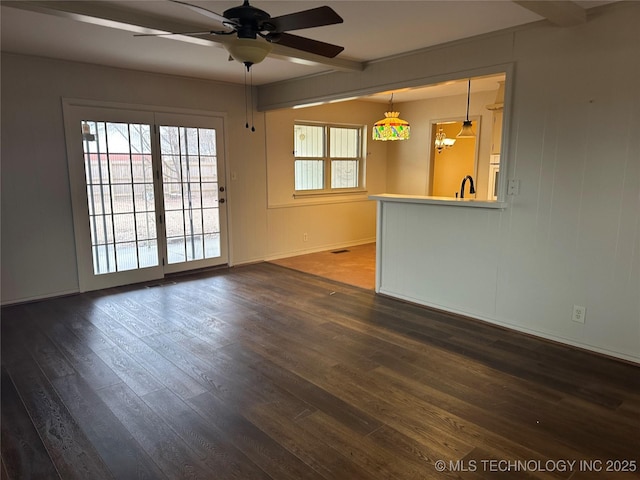 empty room featuring beamed ceiling, dark wood-type flooring, and ceiling fan with notable chandelier