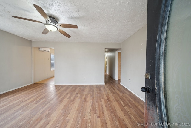 spare room with a wall mounted air conditioner, ceiling fan, light hardwood / wood-style floors, and a textured ceiling