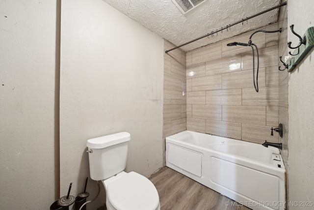 bathroom with tiled shower / bath combo, toilet, wood-type flooring, and a textured ceiling