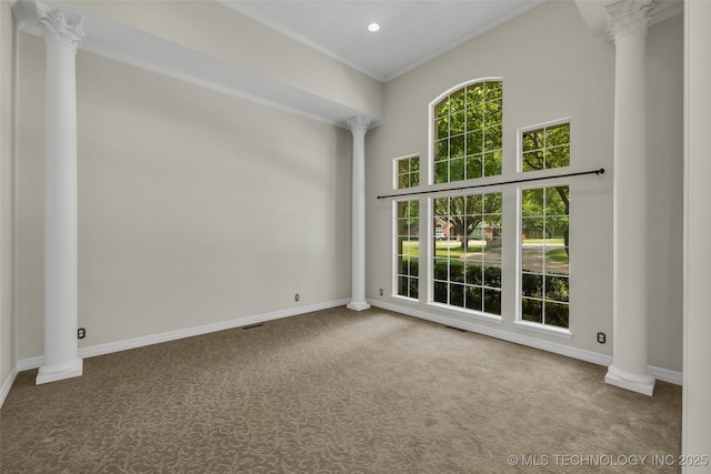 empty room featuring carpet flooring, baseboards, crown molding, and ornate columns