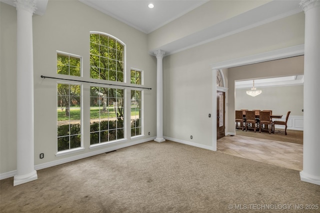 carpeted empty room featuring a high ceiling, ornate columns, ornamental molding, and a notable chandelier